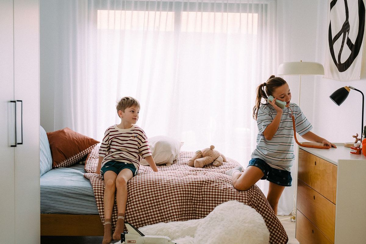 A girl chatting on the Waffle Home handset in a bedroom while her brother sits on the bed.