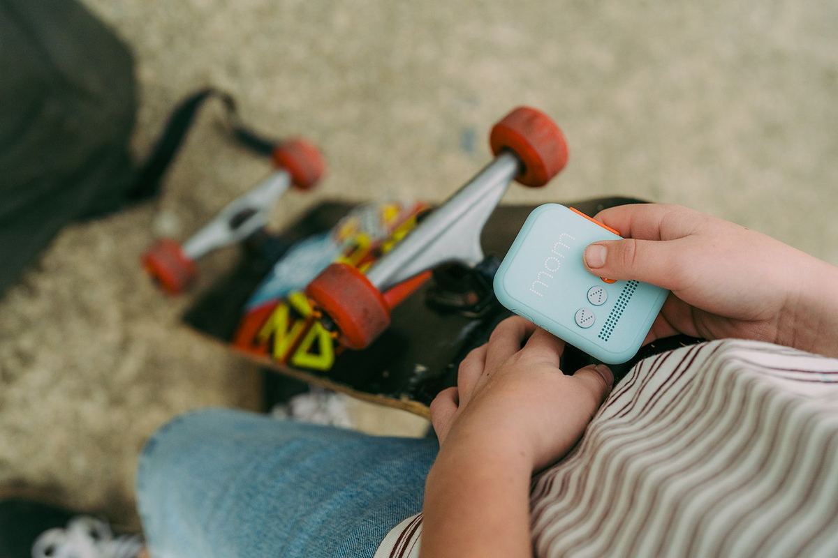 A child sitting beside a skateboard, holding a mint green Waffle Go phone in one hand.