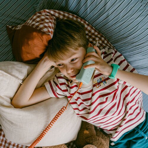 Boy lying on his bed talking on a Waffle kids phone